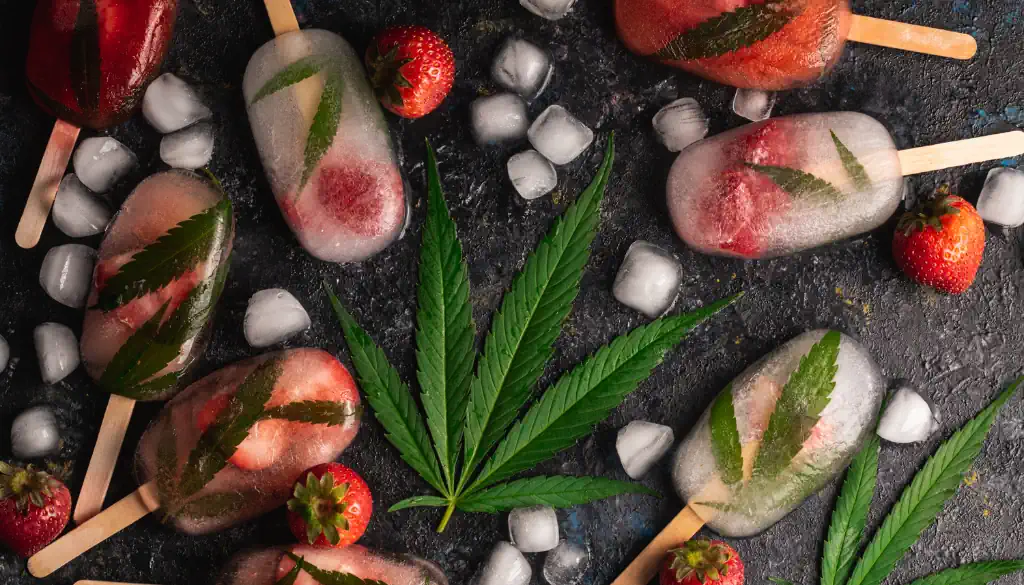 Ein appetitlich gefüllter Eisbecher mit einer großen Kugel Erdbeereis, die mit feinen Tropfen CBD-Öl durchzogen ist und dadurch einen subtilen Glanz erhält. Das Eis wird von frischen Erdbeerscheiben und einem winzigen Hanfblatt garniert, das die besondere Zutat des Desserts hervorhebt. Im Hintergrund sieht man ein sommerliches Setting mit grünen Feldern und einem klaren Himmel, was die Natürlichkeit und Frische der Zutaten unterstreicht.